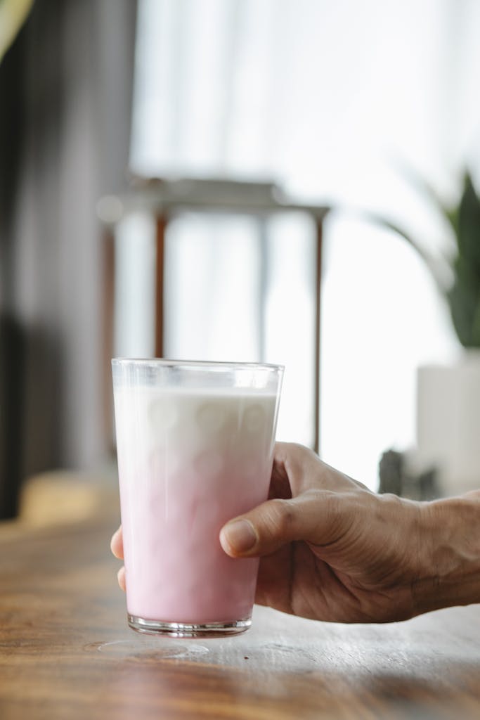 Crop unrecognizable person showing ornamental glass of delicious protein milkshake in house in daylight